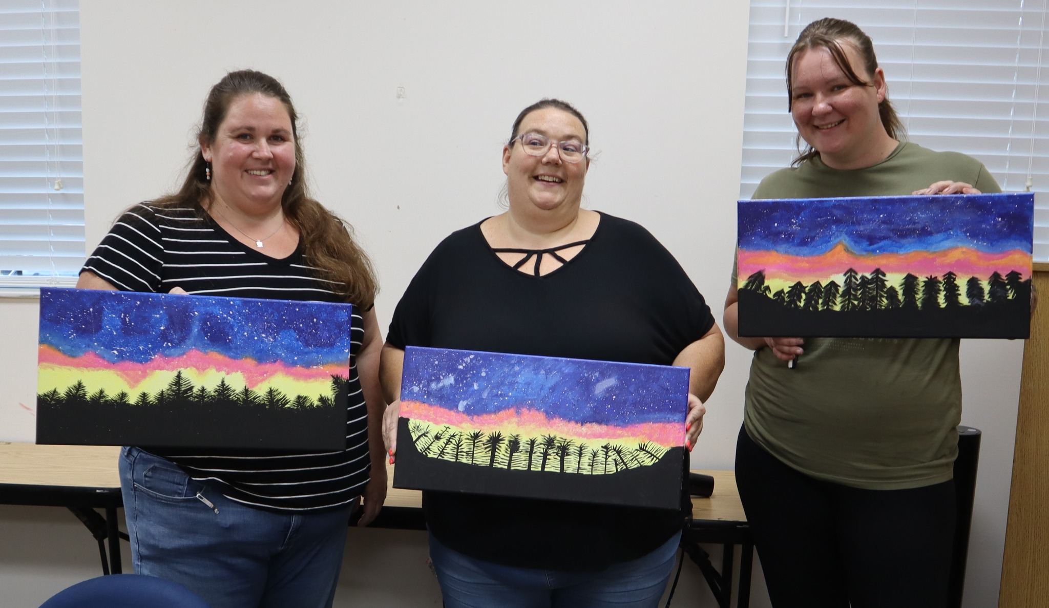 3 women hold up art work created at a library program